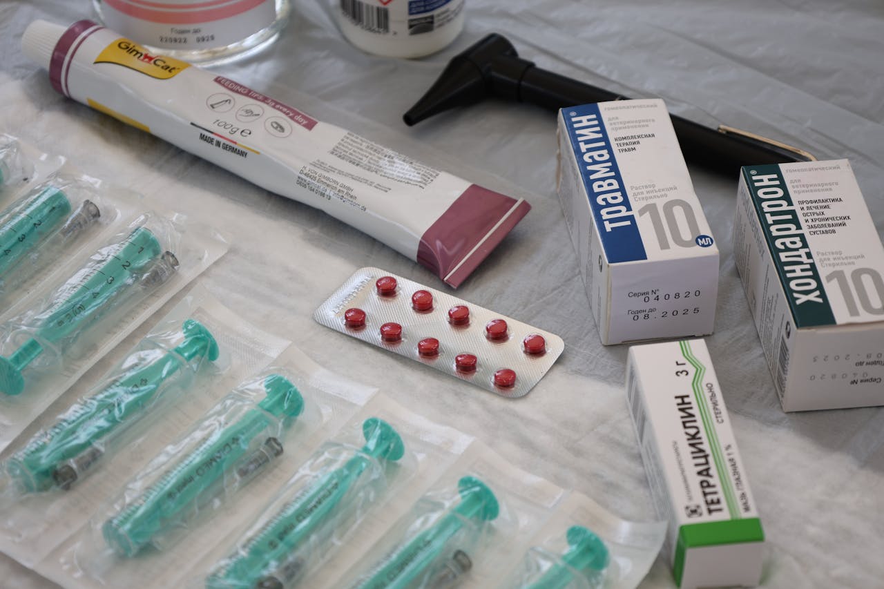 hero-img-01 Flat lay of medical supplies including syringes, pharmaceuticals, and an otoscope on a table.